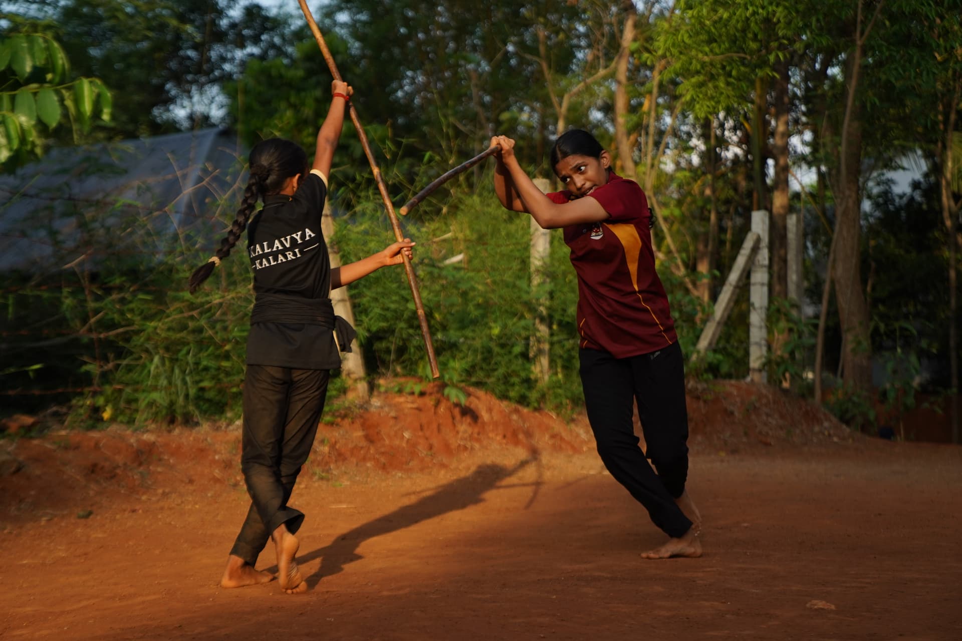 Two students practising long staff outdoors at Ekalavya Kalari